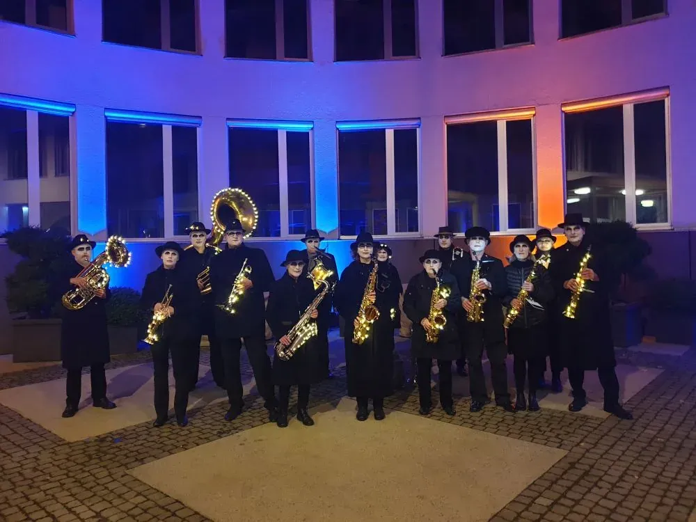 Lauter Blech beim Lichtertreiben 2021 — die fünfzehnköpfige Blechbläser-Band mit Saxophonen, Trompete und lichtgeschmückten Instrumenten vor blau-orange illuminierter Fassade